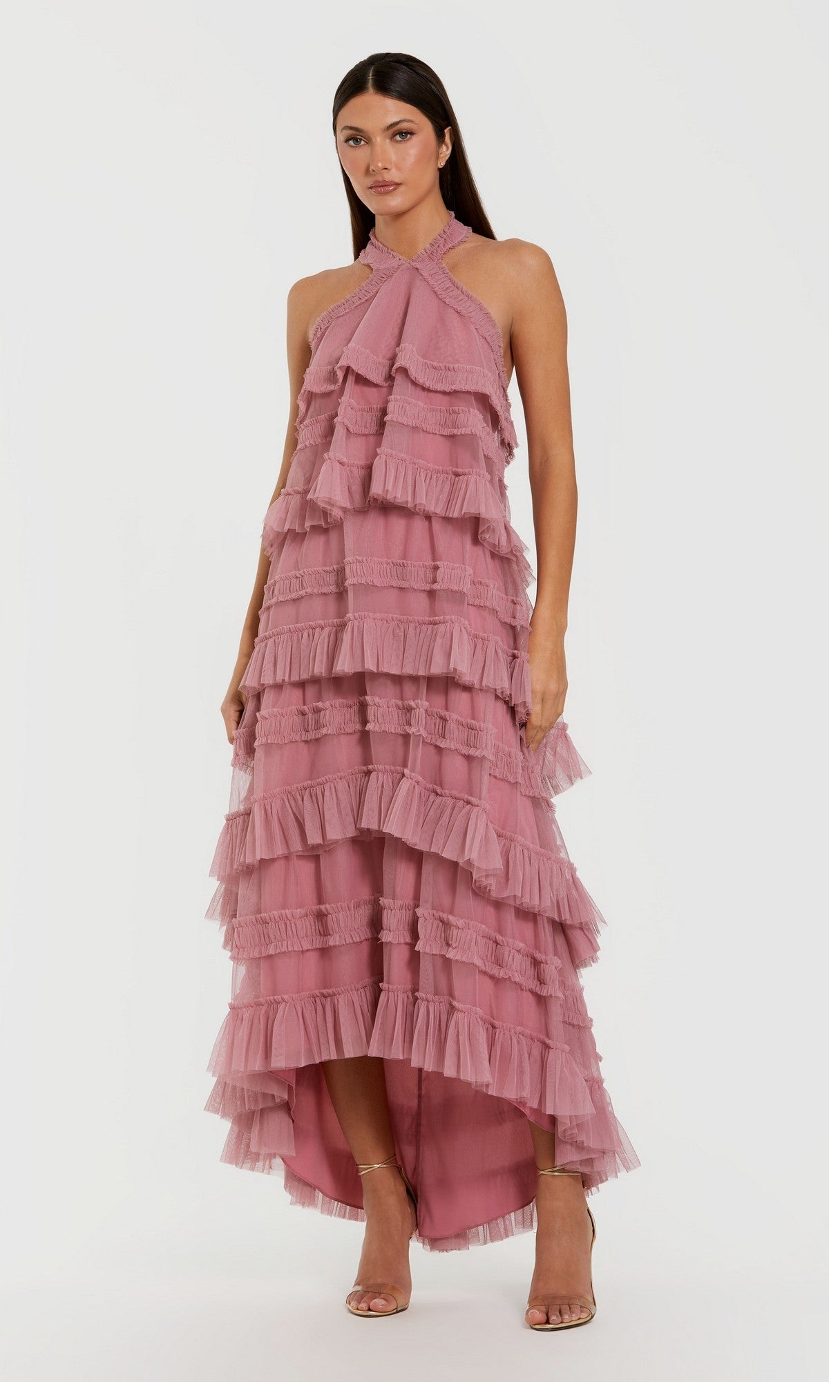 A woman wearing the Mac Duggal 8276 Tea-Length Party Dress in roseโa sleeveless, high-neck design featuring ruffled tiers and a dramatic high-low hemlineโstands in neutral heels against a plain light background.